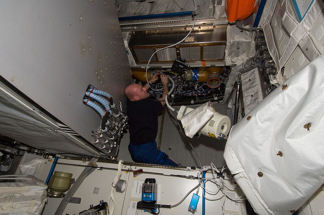 André Kuipers uses a vacuum cleaner on the Columbus ventilation systems (Credit: NASA)