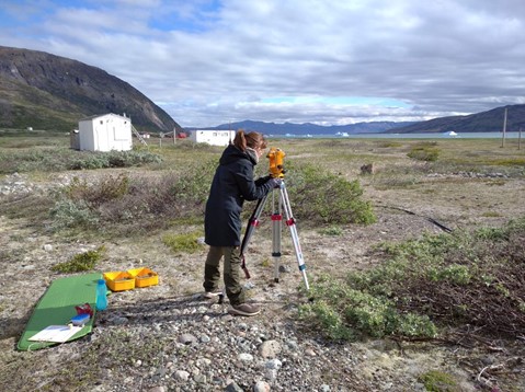 Marie taking measurements with the theodolite. Ice bergs float down the fjord in the distance. (DTU Space-Audrey Schillings)