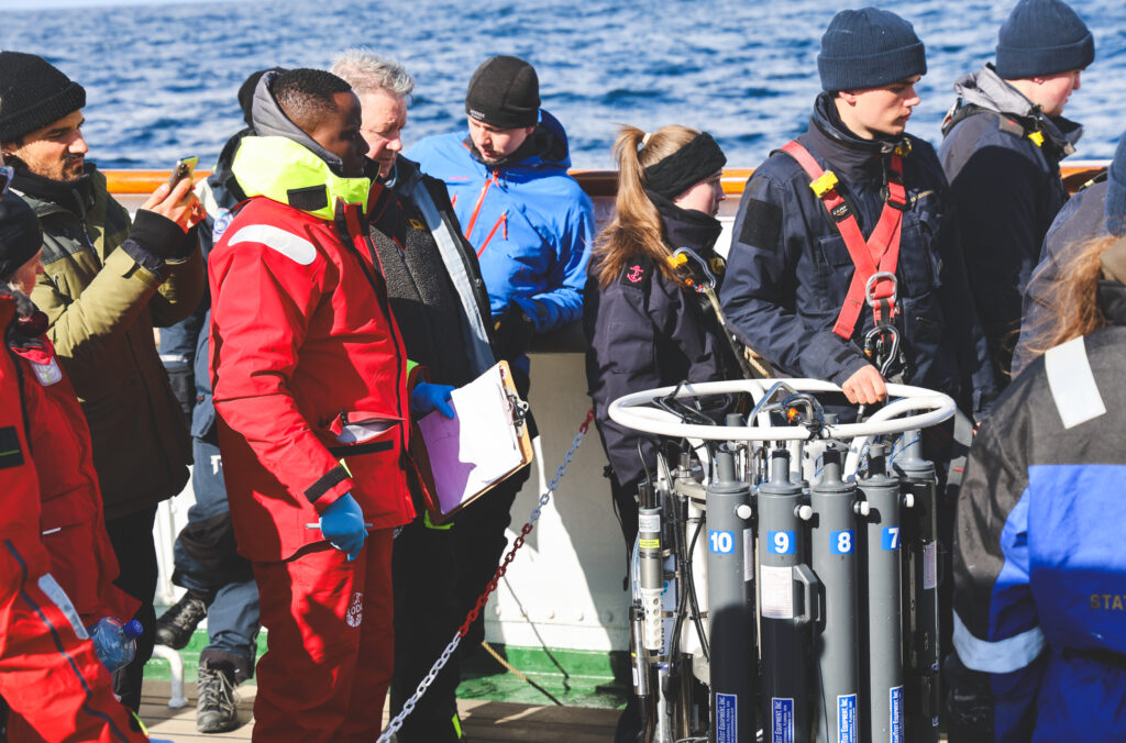 Deck crew getting ready to drop the conductivity, temperature and depth rosette and students following the process closely. (Ocean Media Lab)