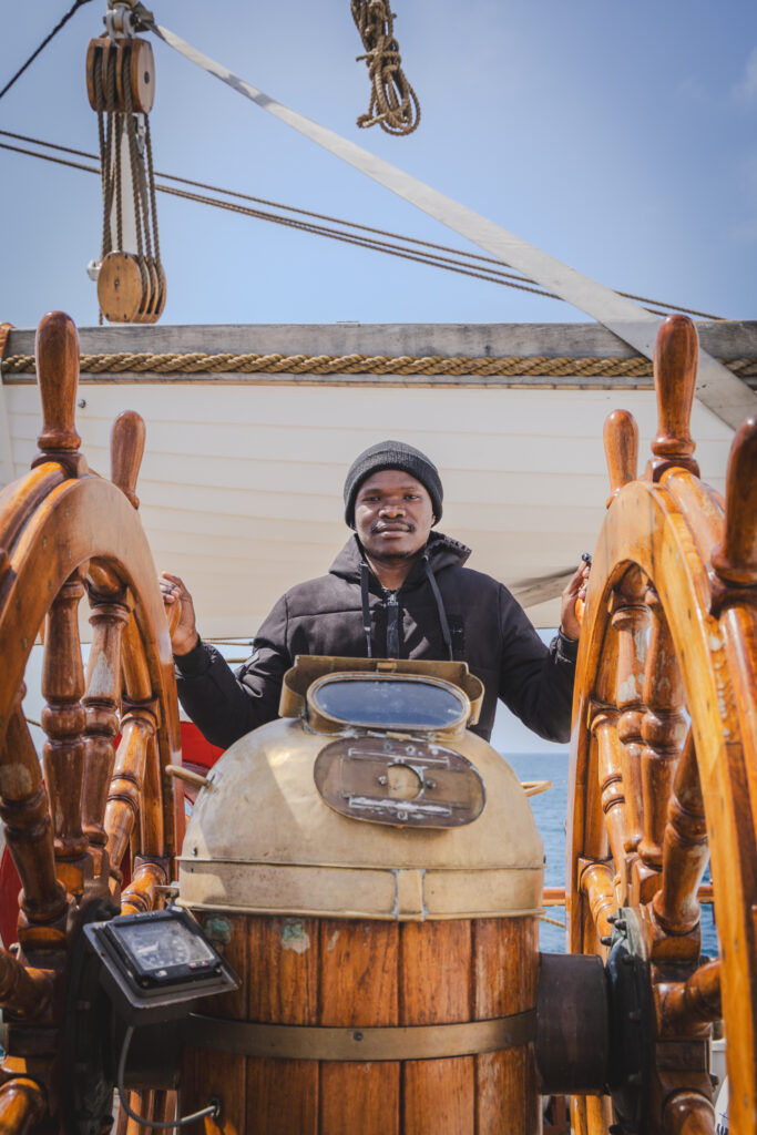 Student Walter Okinyi Ogutu takes the helm as part of the rotating watch schedule, steering through deep Atlantic waters. (Ocean Media Lab)