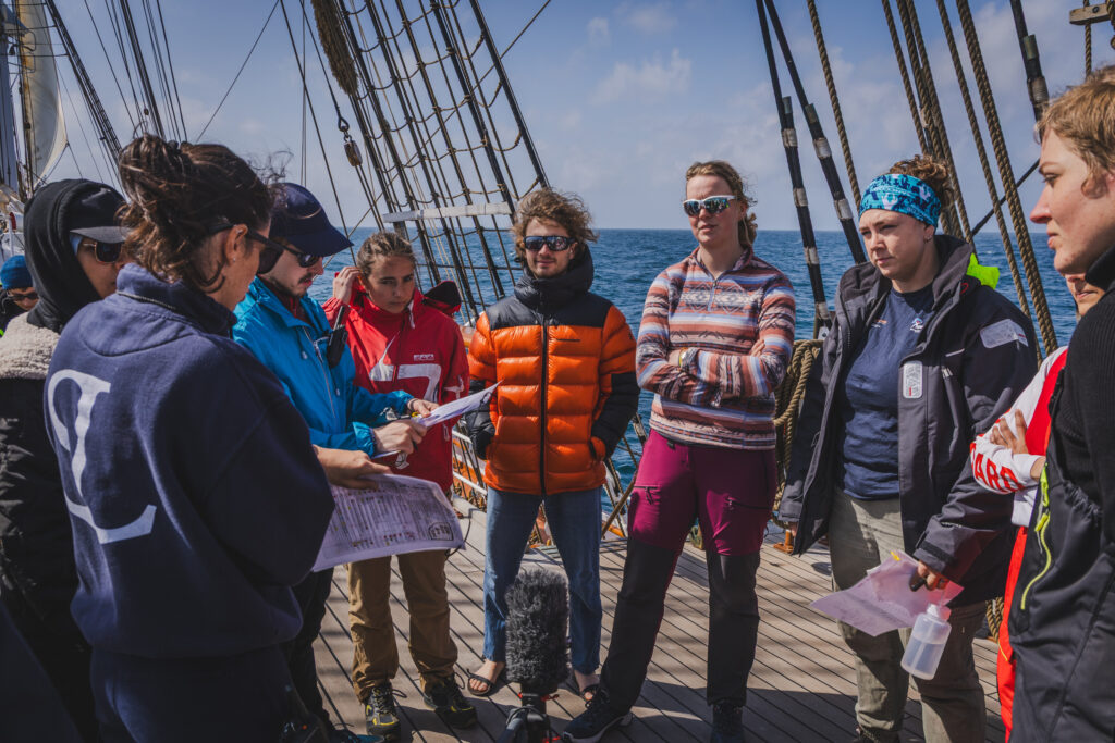 The day begins with a coordination meeting led by the station manager. Students gather around to review satellite data, safety procedures and roles for the upcoming CTD deployment at the Porcupine Abyssal Plain. (Ocean Media Lab)