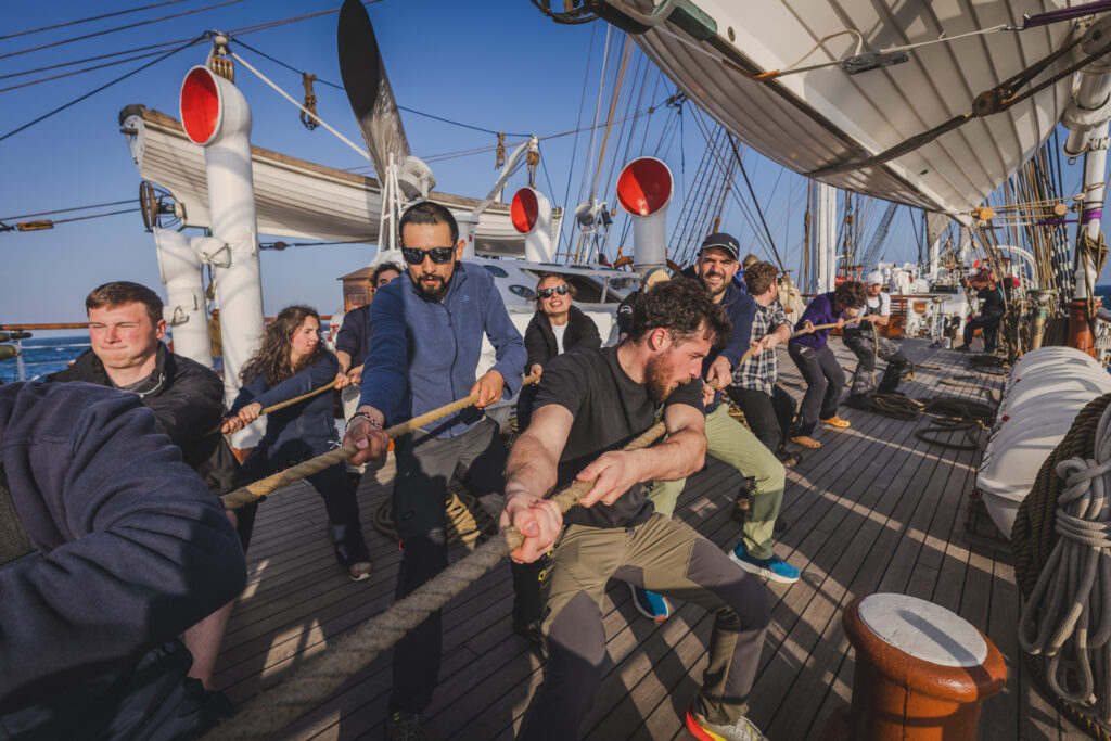 Pulling together, students and crew members adjust rigging lines. Just as science requires collaboration, so too does navigating a tall ship through shifting winds and waves. We can see Astronaut Pablo Àlvarez blending in with the students. (Ocean Media Lab)
