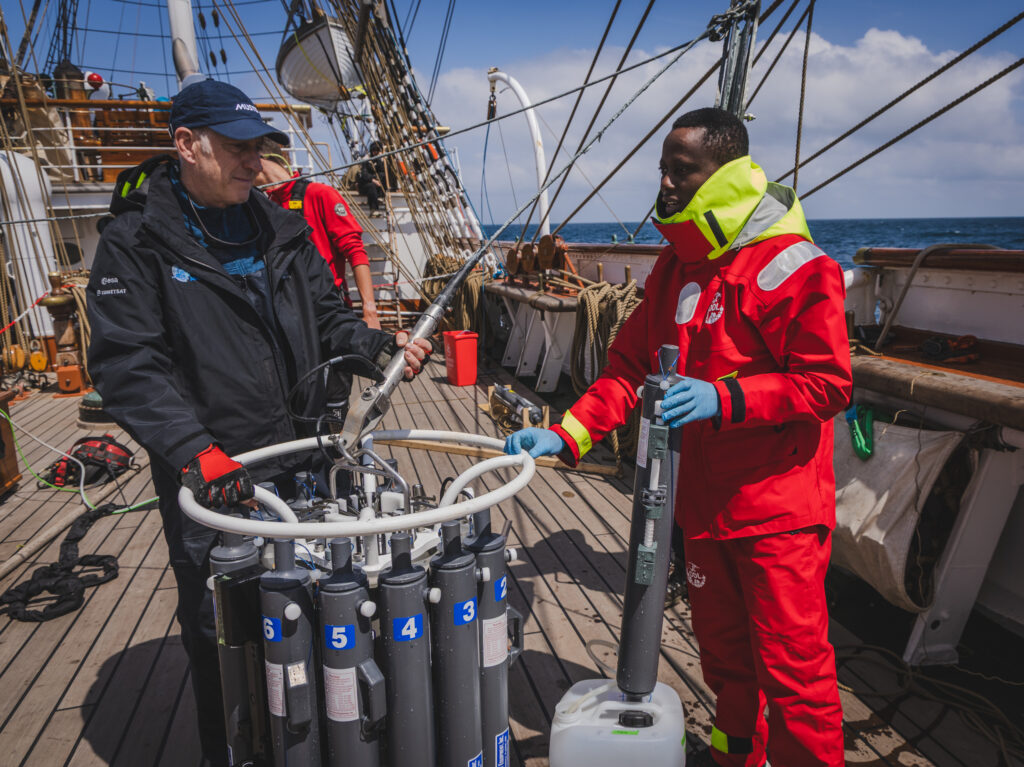 Mark Drinkwater, who heads ESA’s Mission Science Division, and student Unyime Umoh work together to extract water from the rosette’s sampling bottles. The data collected will be matched to satellite readings, completing the satellite-to-sea cycle in real time. (Ocean Media Lab)