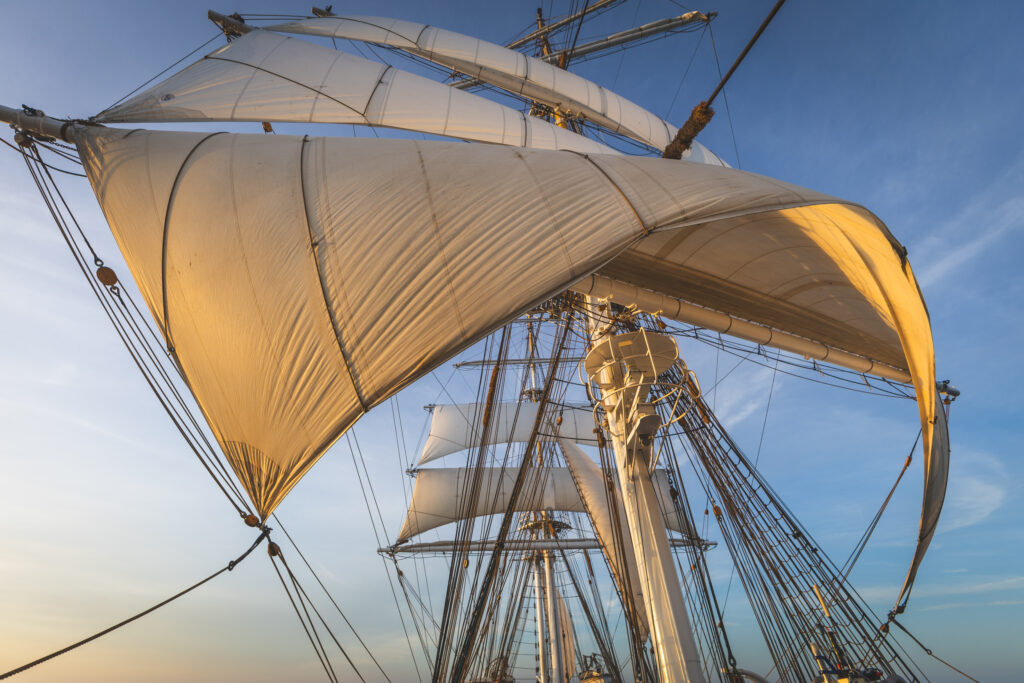 The sails aglow with the last light of day. Like satellite images that capture wind patterns from orbit, here the canvas tells its own story of direction, force and flow. (Ocean Media Lab)