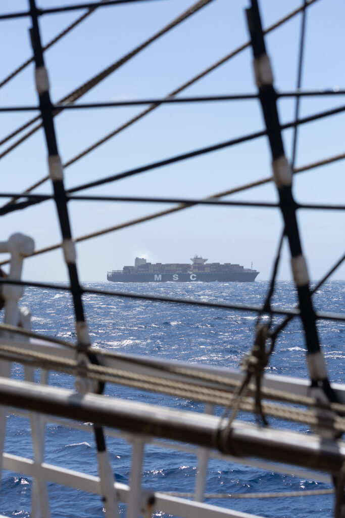 A modern container ship crosses the horizon signals that the historic tall ship is getting closer to civilization after being away from it all at sea. (Ocean Media Lab)