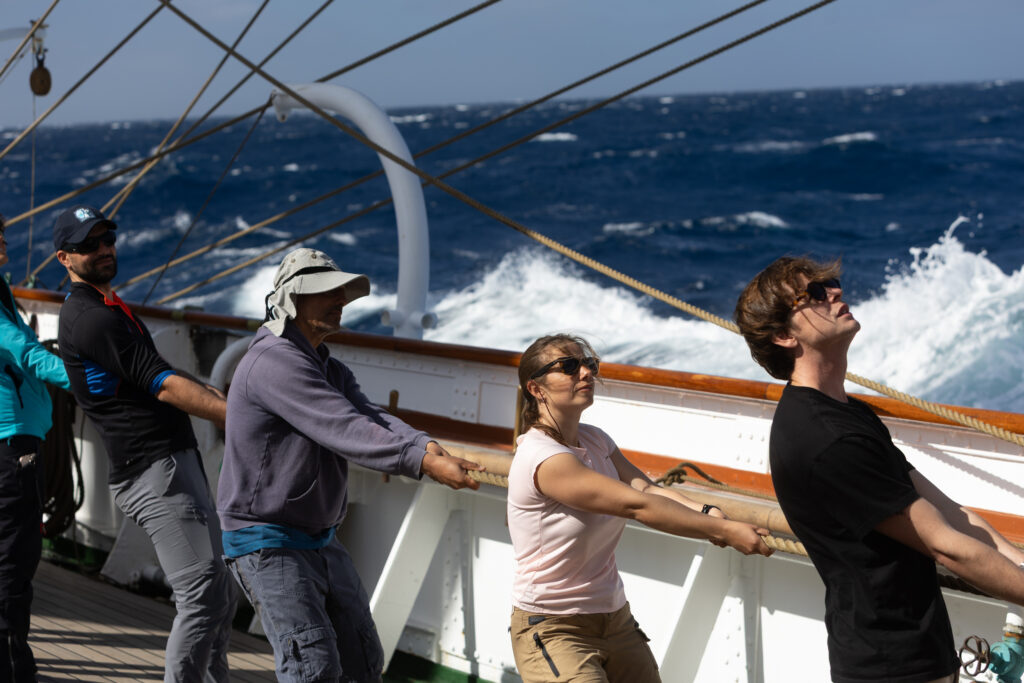 An astronaut, lecturers and students haul lines together in strong winds, learning by doing at sea. (Ocean Media Lab)